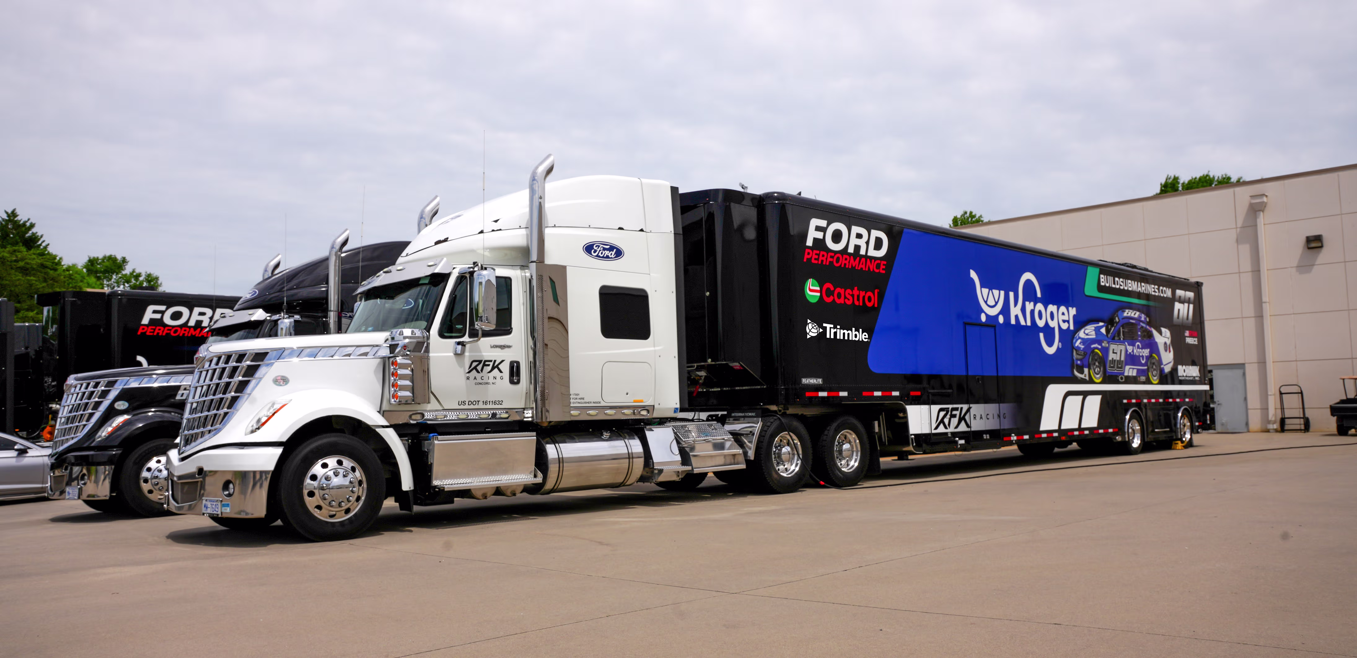 Front three-quarter view of an RFK Racing hauler parked outside a motorsports facility, with branding visible on the trailer.