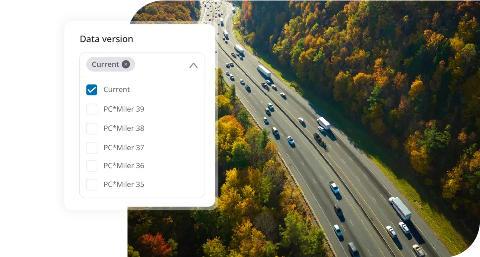 An aerial view of trucks on a multi-lane highway bordered by autumn trees, overlaid with a PCMiler software menu for selecting data versions.