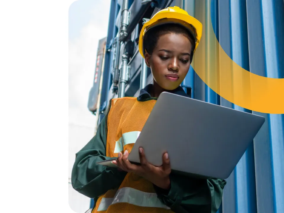 Warehouse worker using a laptop to manage inbound logistics and supplier collaboration near freight containers.
