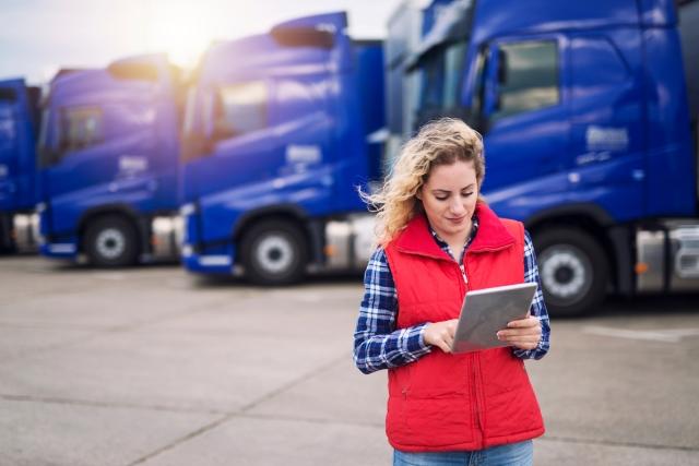 Woman working on a tablet with semi trucks behind her