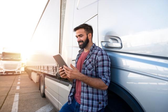 Man leaning against a semi working on a tablet