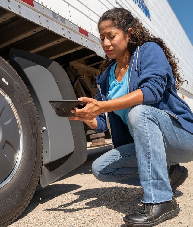 Driver DVIR on side of truck inspecting tire with Tablet